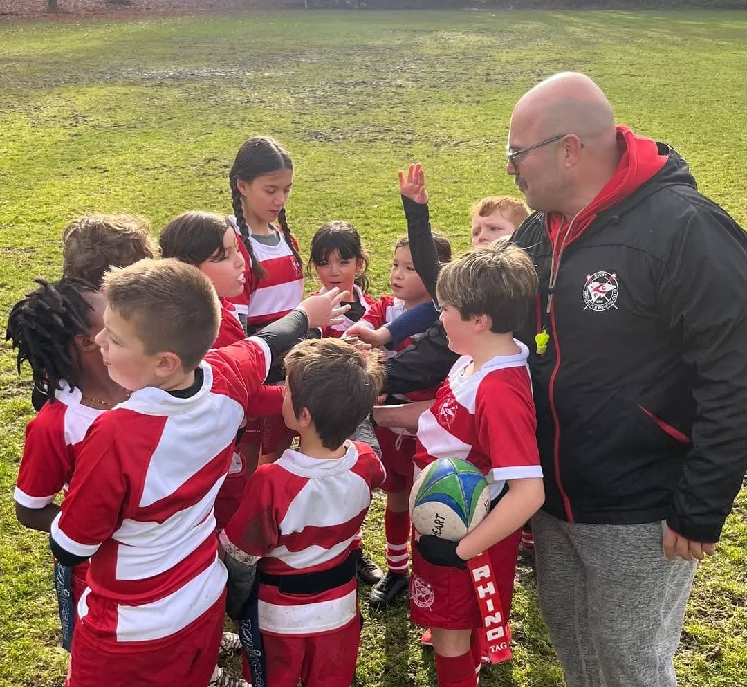 Chris Seyler coaching VRC Rugby Minis in a huddle on the pitch at Brockton Oval in Stanley Park, Vancouver